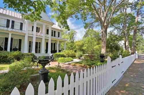A charming white house with a porch, surrounded by lush greenery and a white picket fence on a sunny day.