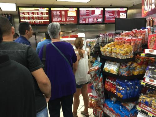 A group of people waiting in line at a fast food counter, with snacks displayed on the side.
