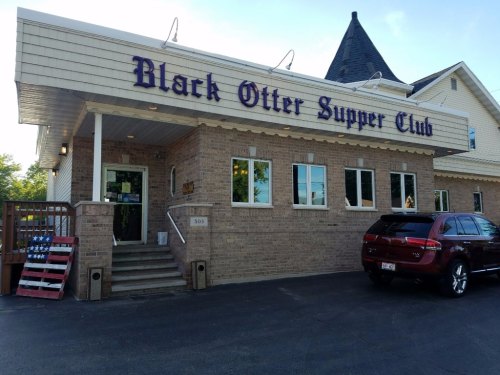 Exterior of the Black Otter Supper Club, featuring a brick facade, large windows, and a parked vehicle in front.