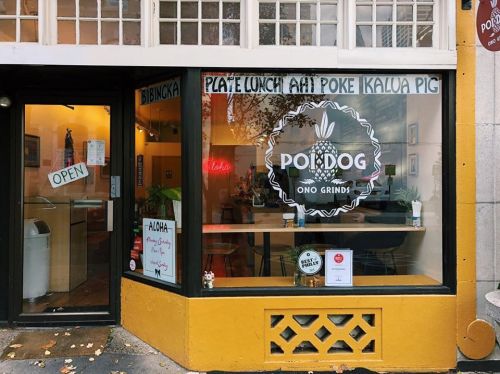 A storefront with a large sign reading "POI DOG" and "OPEN," featuring a menu of Hawaiian dishes.