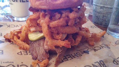 A towering burger with crispy onion rings, pickles, and layers of beef, served on parchment paper.