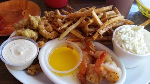 A plate of fried shrimp, coleslaw, fries, and dipping sauces on a wooden table.