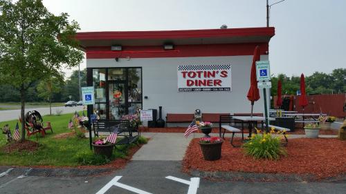 Exterior of Totin's Diner with a red and white sign, benches, flowers, and American flags in front.