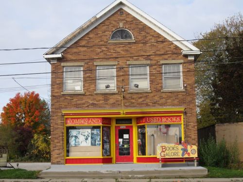 A brick building with large windows, featuring a colorful sign for "Comics and Used Books" and "Books Galore."