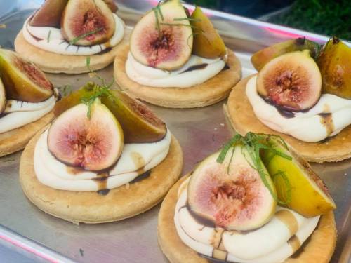 Delicious fig tarts topped with fresh figs, creamy filling, and drizzled with chocolate sauce on a silver tray.