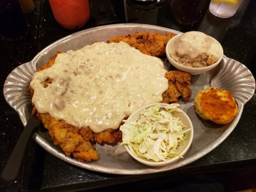 A large platter featuring fried chicken smothered in gravy, with sides of mashed potatoes, coleslaw, and a biscuit.