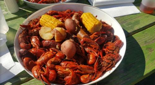 A large platter of boiled crawfish, potatoes, corn, and sausage on a wooden table.