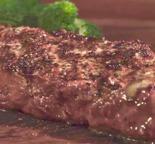 Close-up of a perfectly cooked steak with a seared crust, accompanied by fresh broccoli on a wooden surface.