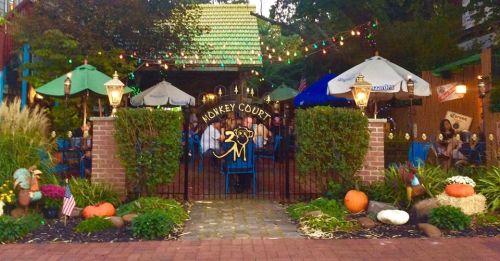 A charming outdoor dining area with colorful lights, pumpkins, and greenery, featuring a sign that reads "Monkey Court."