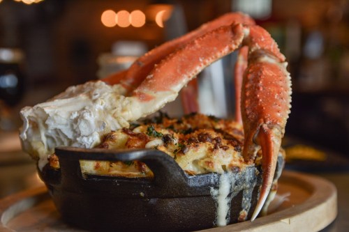 A cast iron dish filled with creamy seafood pasta topped with a large crab claw.