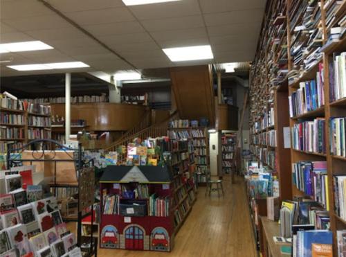 A cozy bookstore interior with tall bookshelves, a wooden staircase, and a colorful children's play area.