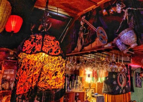 A cozy bar interior featuring a colorful lamp, hanging glassware, and eclectic decor on the walls.
