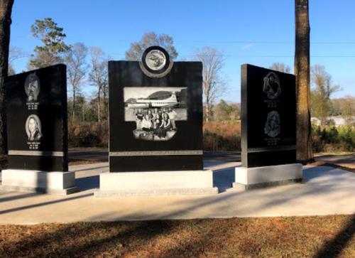 A memorial with three black granite panels featuring engravings and a central image of a plane and people.