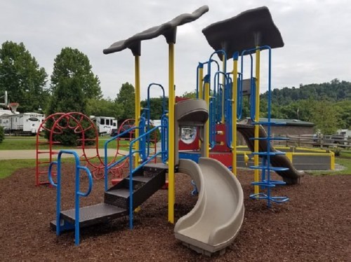 Colorful playground equipment with slides, climbing structures, and steps, surrounded by mulch and greenery.