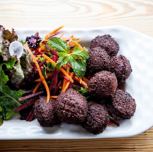 A plate of crispy falafel balls served with a colorful salad of shredded carrots, beets, and fresh mint.