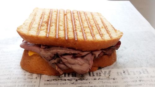 A toasted sandwich filled with roast beef and melted cheese, resting on a sheet of paper.