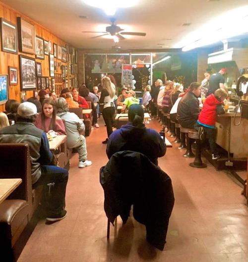 A busy diner filled with people sitting at booths and the counter, with warm lighting and wooden decor.