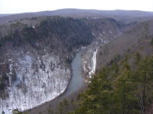 A scenic view of a winding river surrounded by snow-covered hills and trees in a winter landscape.