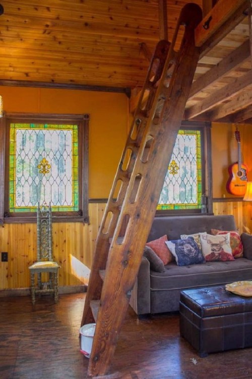 A cozy interior featuring a wooden ladder, stained glass windows, a sofa with cushions, and a guitar on the wall.