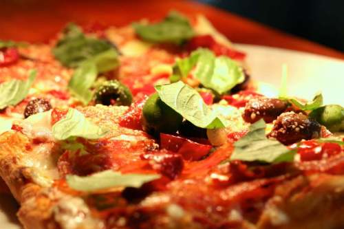 Close-up of a delicious pizza topped with fresh basil, olives, and colorful vegetables on a wooden table.
