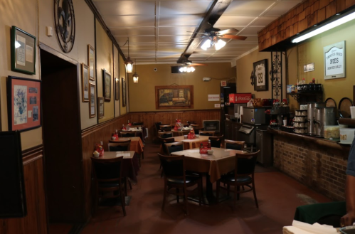 Cozy restaurant interior with wooden tables, chairs, and a counter featuring drinks and decor on the walls.