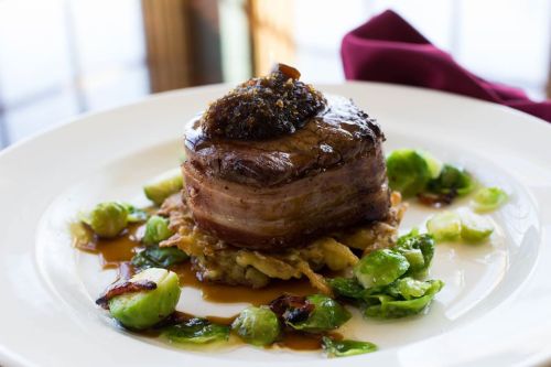 A gourmet dish featuring a thick cut of meat topped with a savory sauce, served on a bed of greens and Brussels sprouts.