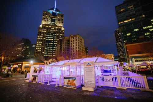 A city square at night featuring illuminated tents and a tall building in the background.