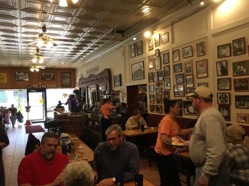 A bustling restaurant interior with patrons dining, walls adorned with framed photos, and staff serving food.