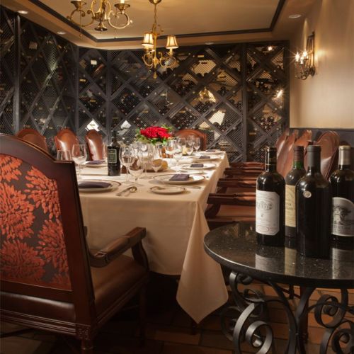 Elegant dining room with a long table set for a meal, surrounded by leather chairs and a wine display in the background.