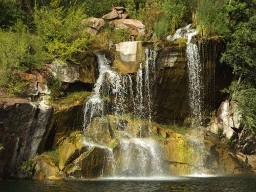 A serene waterfall cascading over rocky cliffs, surrounded by lush greenery and reflecting in a calm pool below.