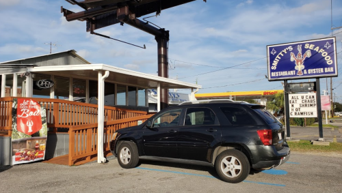 A black SUV parked outside Smithy's Seafood restaurant, featuring a sign for all-you-can-eat crabs and shrimp.