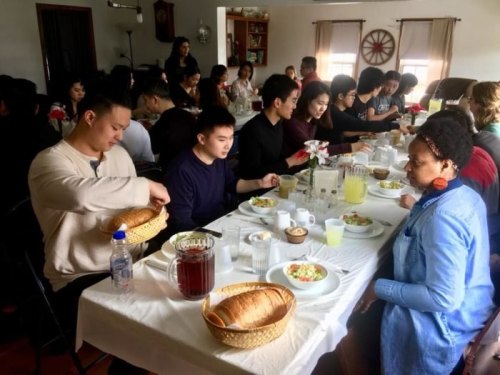 A diverse group of people enjoying a meal together at a long table, with food and drinks served.