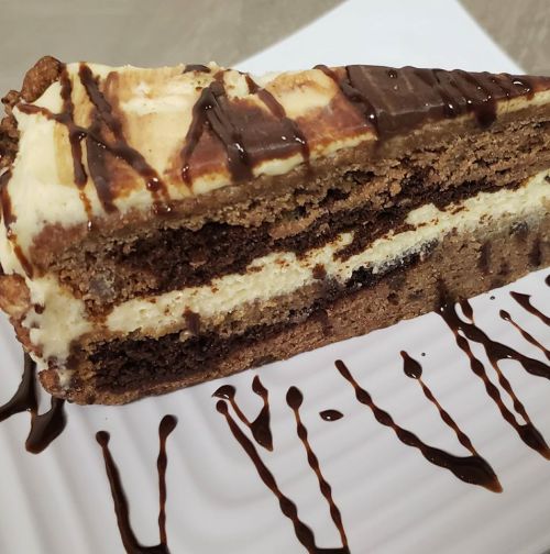 A slice of layered chocolate cake with cream filling, drizzled with chocolate sauce on a white plate.