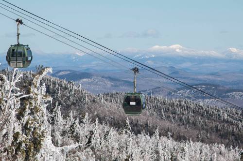 Two gondolas glide over a snowy landscape, with distant mountains visible under a clear blue sky.