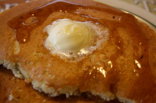 A close-up of a fluffy pancake topped with a pat of butter and drizzled with syrup.