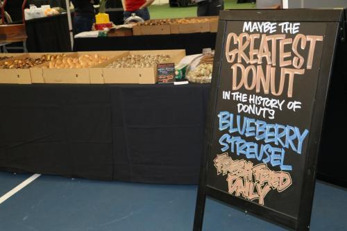 A display of assorted donuts with a sign promoting "the greatest donut" - blueberry streusel, fresh baked daily.