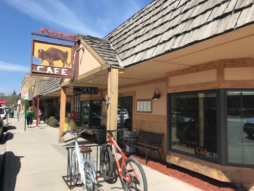 A quaint café with a buffalo sign, outdoor seating, and bicycles parked outside on a sunny day.
