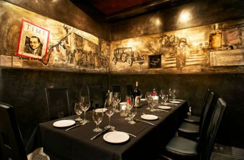 A dimly lit restaurant with a long table set for dinner, featuring vintage wall art and a framed photo.