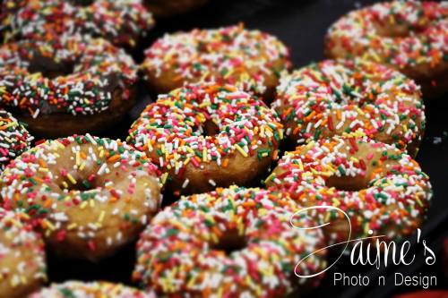 A close-up of colorful donuts topped with sprinkles, arranged on a dark surface.