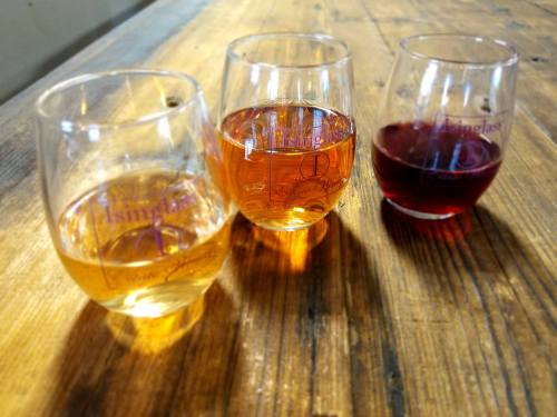 Three wine glasses with different colored wines—golden, pink, and red—on a wooden table.