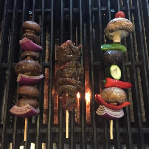 Grilled skewers with mushrooms, beef, and colorful vegetables on a barbecue grill.