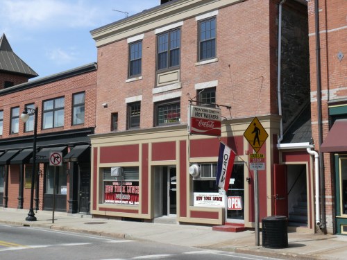A brick building with a sign for "New York Style Hot Wieners" and an "Open" banner, located on a street.