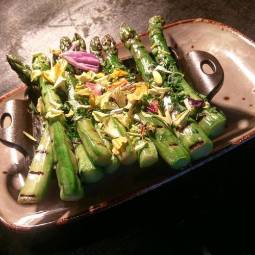 Grilled asparagus topped with colorful edible flowers on a decorative plate.