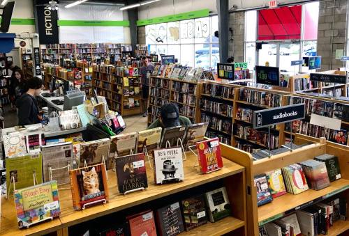 A spacious bookstore filled with shelves of books, featuring a checkout area and a display of audiobooks in the foreground.