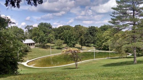 A serene park scene featuring a curved pond surrounded by lush greenery and trees under a partly cloudy sky.