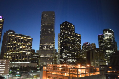 City skyline at dusk, featuring tall buildings illuminated against a deep blue sky.
