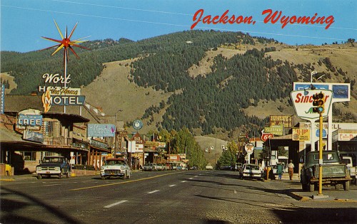 Vintage postcard of Jackson, Wyoming, featuring a street lined with motels and shops against a mountainous backdrop.