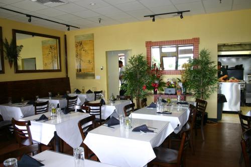 Interior of a restaurant featuring tables with white tablecloths, plants, and a view of the kitchen area.
