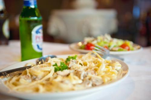 A plate of creamy pasta with herbs, a fresh salad, and a bottle of soda on a table.