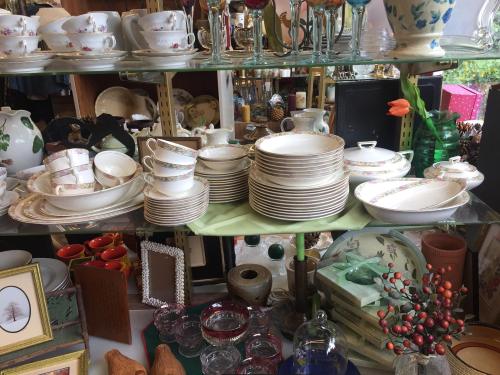 A display of vintage dishware, including plates, cups, and decorative glassware, arranged on shelves.